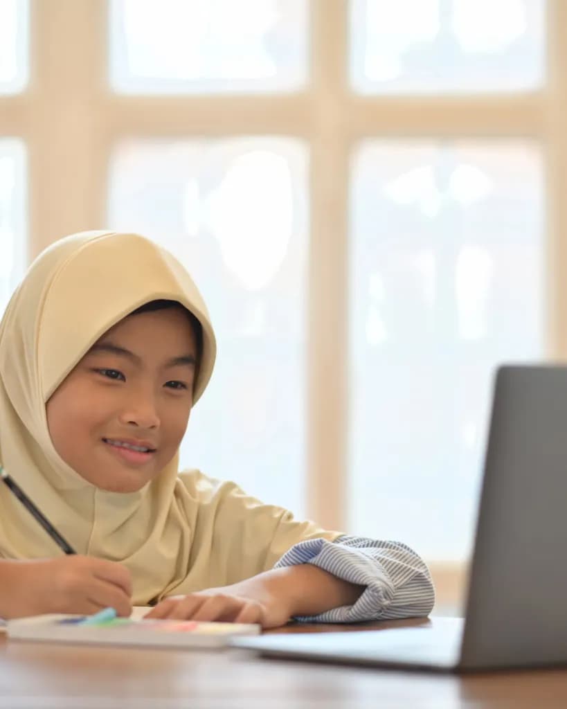 A young student smiling as she works at a laptop